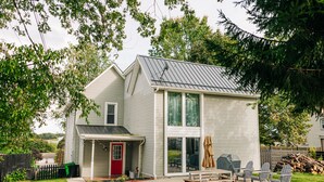 A two-story house with a covered patio, a red door, and a large window.