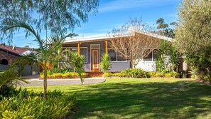 A modern house with a covered porch, a well-maintained lawn, and various plants. - The Anchor - Pet Friendly - 5 Mins Walk to Beach - EV Charging (Callala Beach)