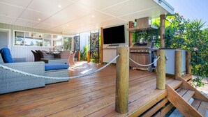 Una terraza de madera con área de estar, una parrilla y una pantalla de televisión.