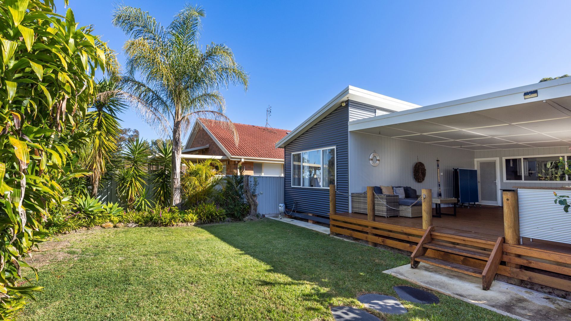 A modern house with a covered patio, a well-maintained lawn, and tropical plants.