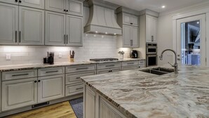 A modern kitchen with white cabinetry, a marble countertop, and built-in appliances including a stove, oven, and sink.