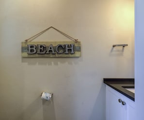 Une salle de bain avec une pancarte en bois sur laquelle est écrit « PLAGE », accrochée au mur.