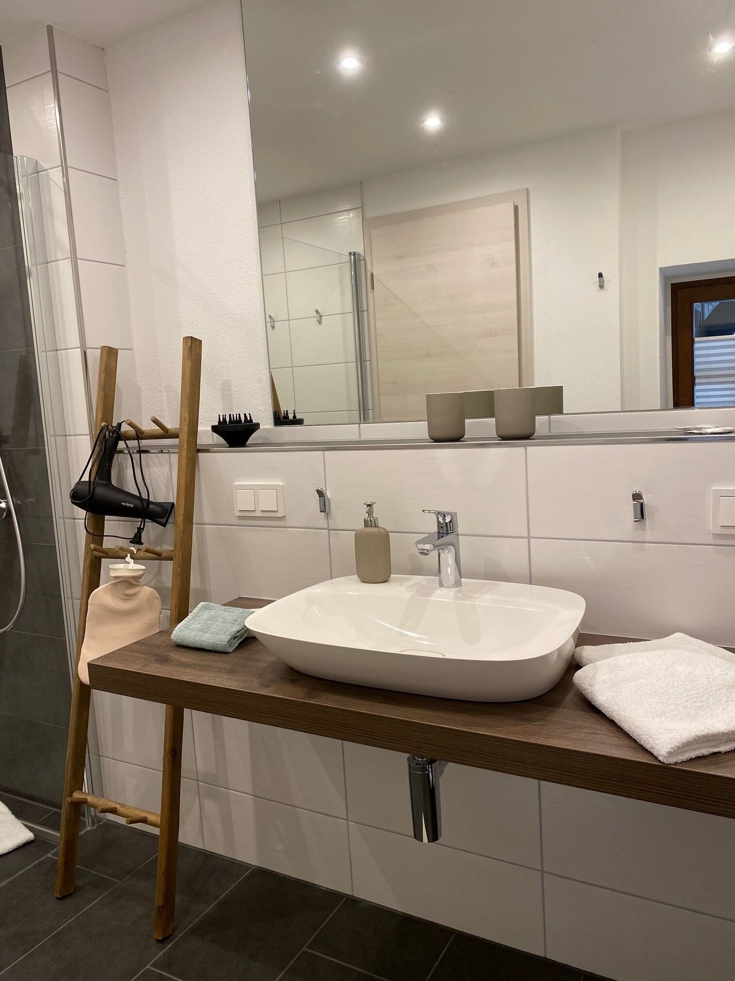 A modern bathroom with a large mirror, a white sink, and a wooden vanity.