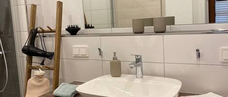 A modern bathroom with a large mirror, a white sink, and a wooden vanity.