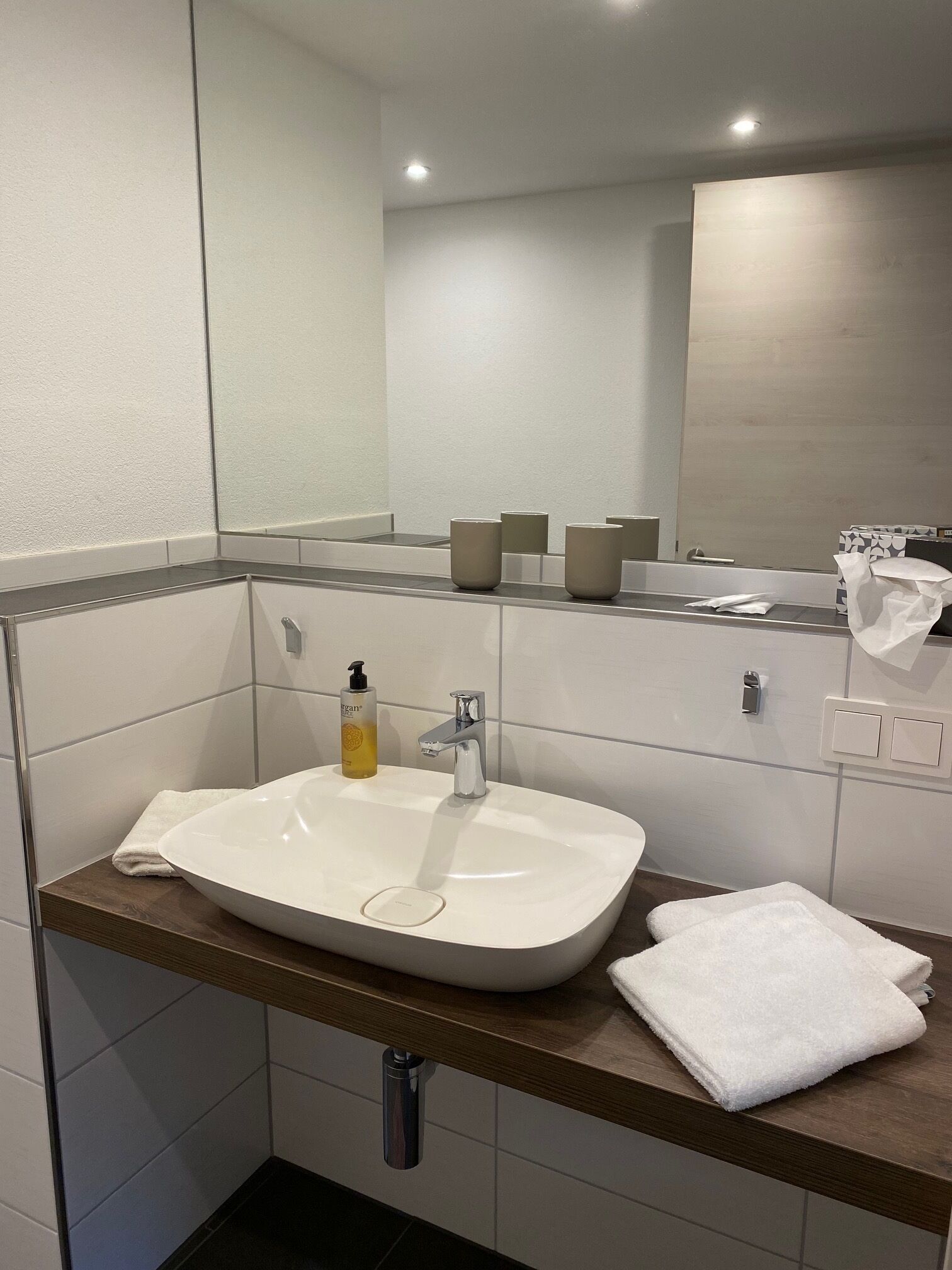 A modern bathroom with a white sink, a mirror, and a towel on the counter.