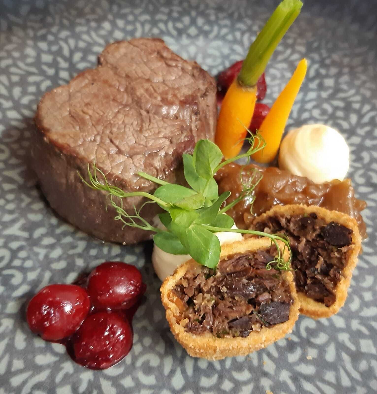 A plate with a slice of beef, a pastry, and some vegetables.