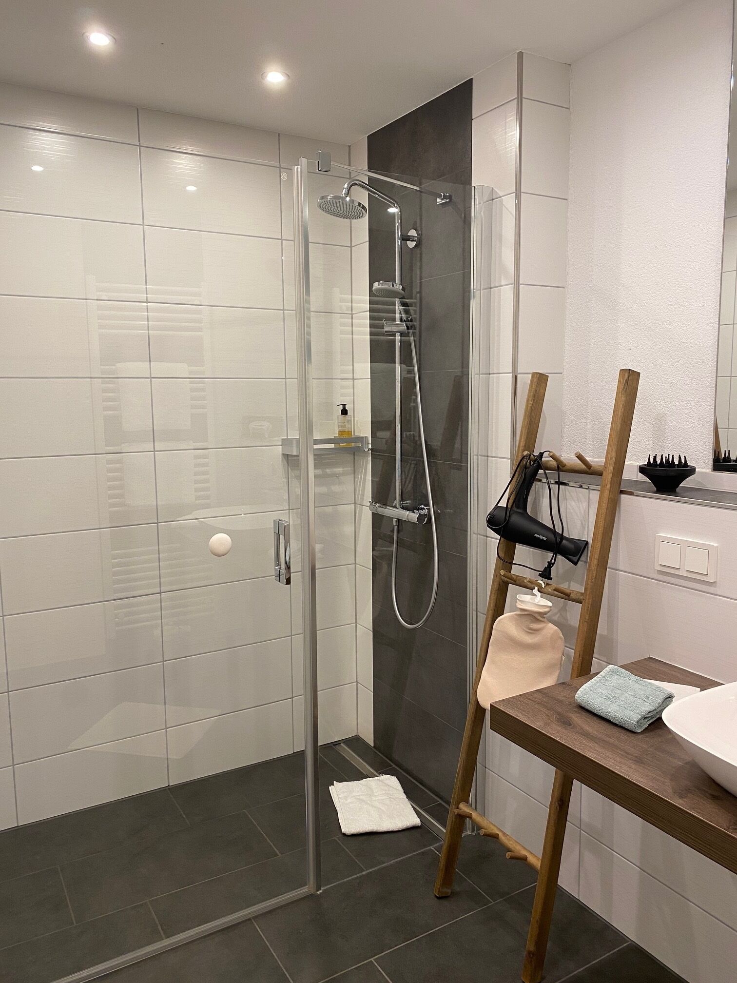 Un baño moderno con ducha acristalada, un tendedero de madera y un lavamanos con espejo.