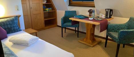 A cozy room with a bed, two chairs, a table, a wooden wardrobe, and a window with a view.