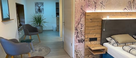 A modern bedroom with a bed, a desk, and a chair. There is a plant and a painting on the wall.