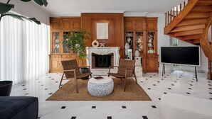 A living room with a fireplace, wooden furniture, and a TV. - The Southern Mansion (Vari-Voula-Vouliagmeni)