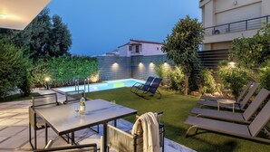 A backyard with a swimming pool, lounge chairs, a table, and a well-maintained lawn. - The Southern Mansion (Vari-Voula-Vouliagmeni)