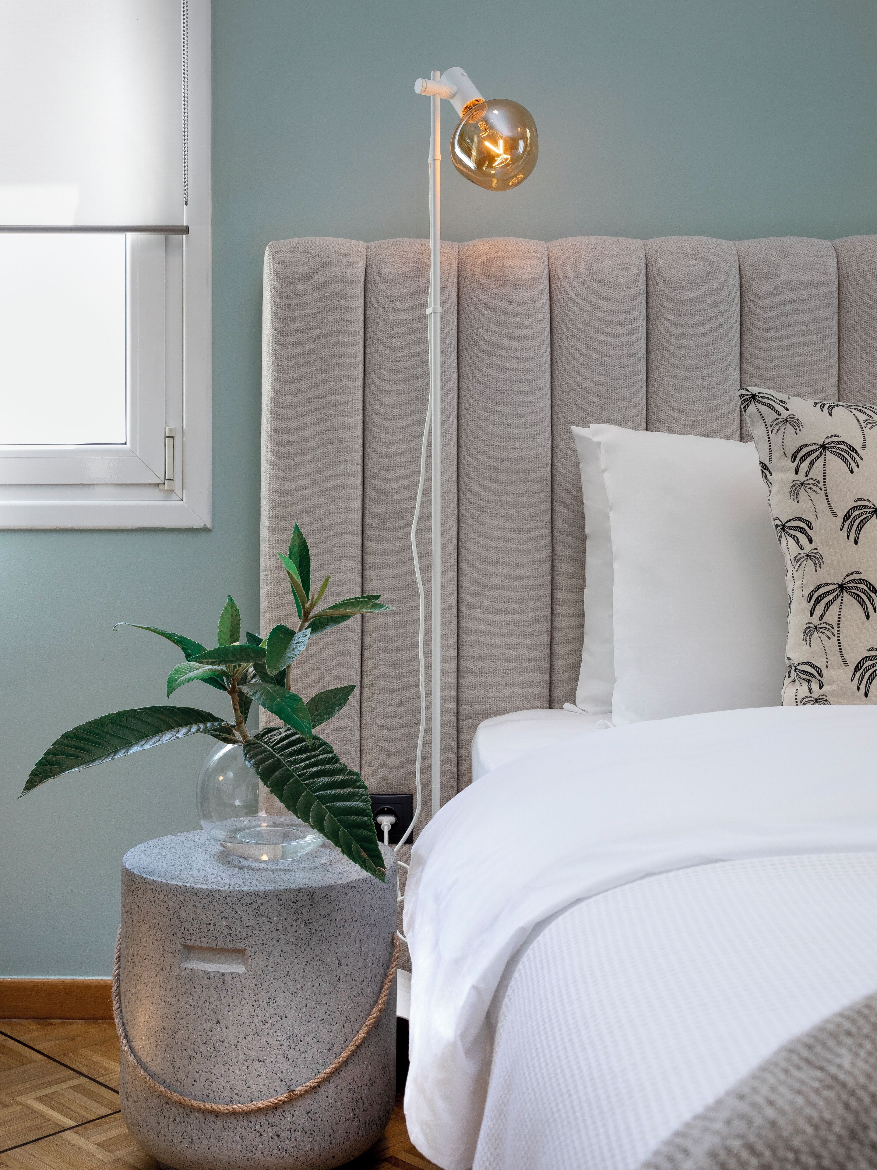 Un dormitorio con una cama, una lámpara de noche, una planta en maceta y una ventana.