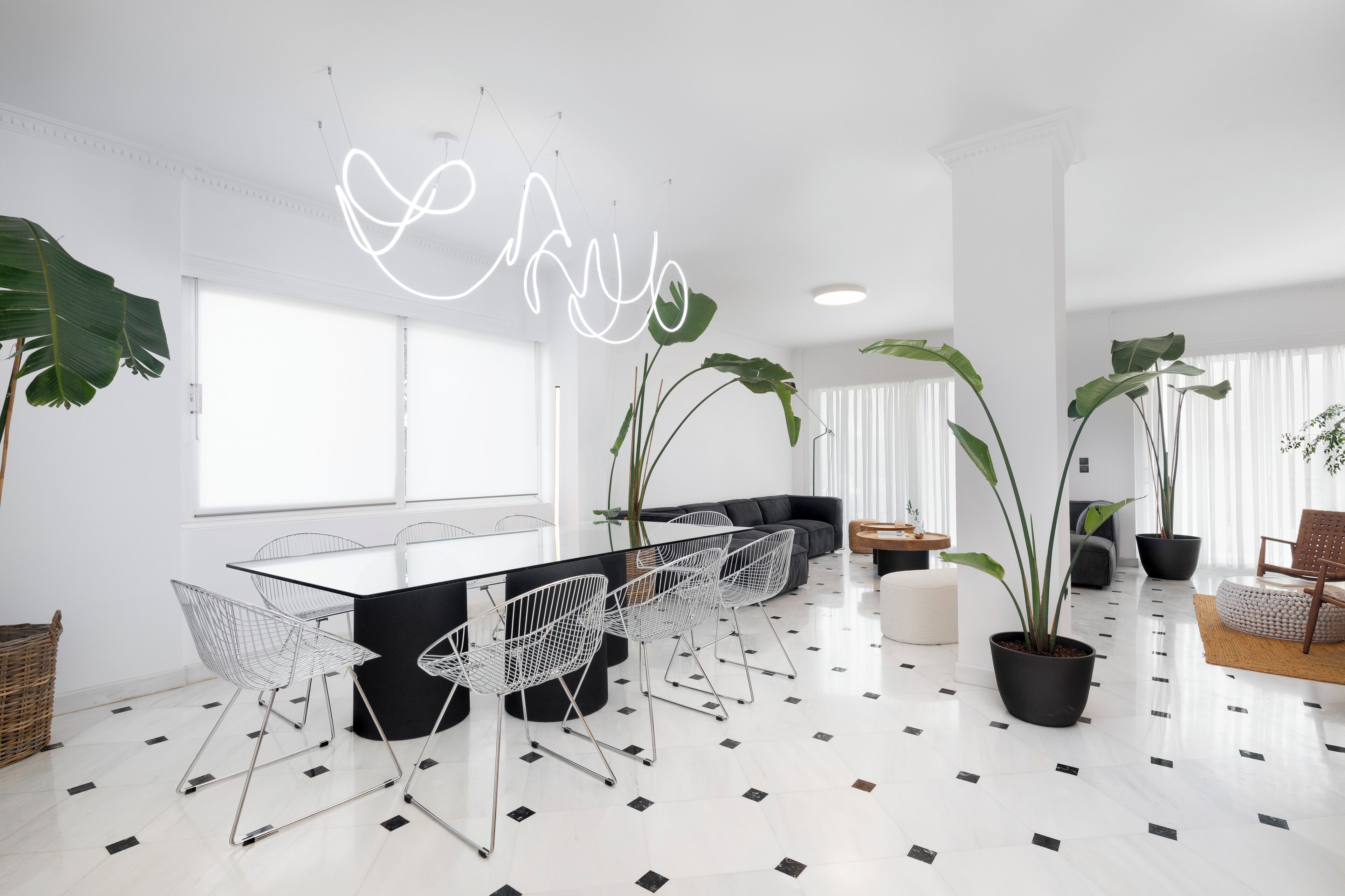 Un espace repas moderne avec une longue table, des chaises blanches et des plantes en pot.