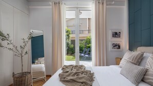 A bedroom with a bed, a bedside table, a mirror, and a view of a balcony with outdoor furniture. - The Southern Mansion (Vari-Voula-Vouliagmeni)