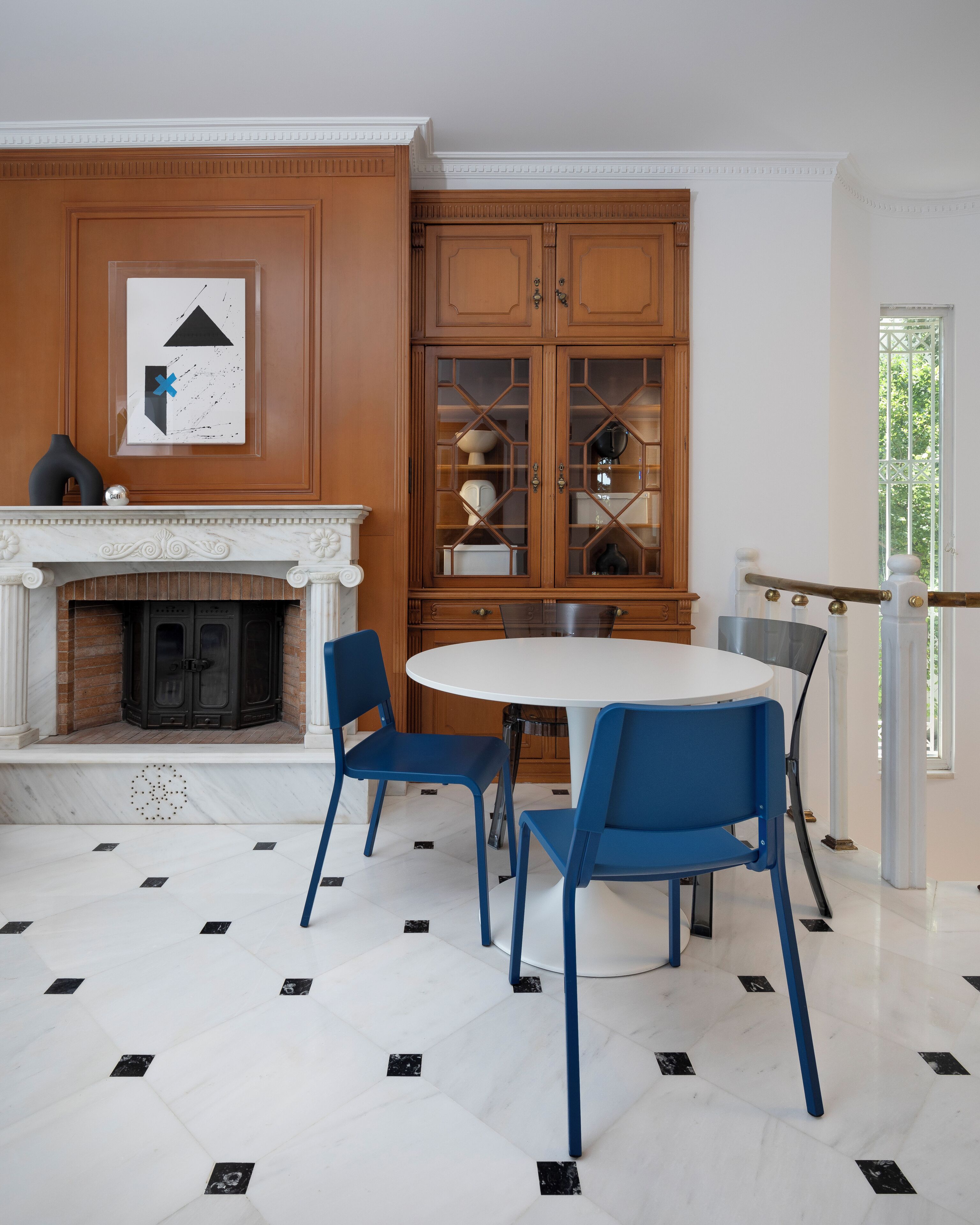 A dining area with a white round table, blue chairs, a wooden cabinet with glass doors, and a fireplace.