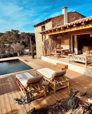 A wooden deck with lounge chairs, a pool, and a stone building with a tiled roof. - New rental with swimming pool  in corsica (Zonza)