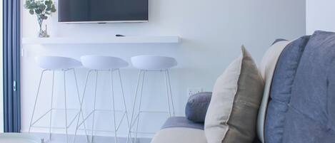 A modern living room with a grey sofa, a flat-screen TV mounted on a white wall, and a small table with a plant.