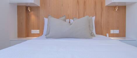Un dormitorio moderno con cabecera de madera, ropa de cama blanca y mesitas de noche con lámparas.