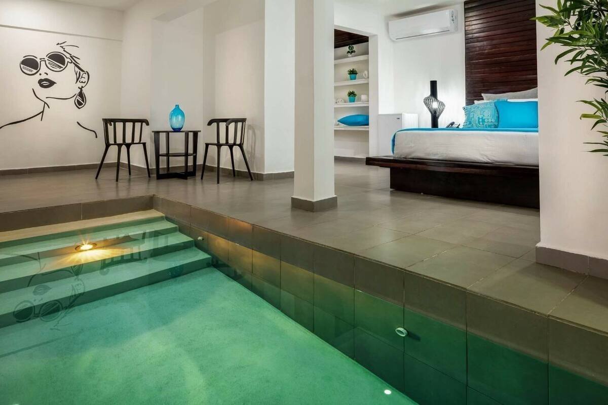 Une chambre d’hôtel moderne dotée d’une piscine à fond de verre, d’un lit avec une literie bleue et d’un décor minimaliste.