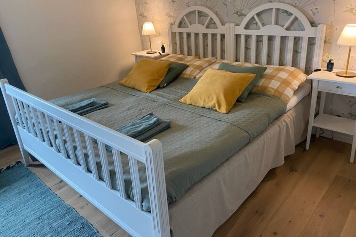 A bed with a white headboard, two bedside tables, and a floral wallpaper pattern.