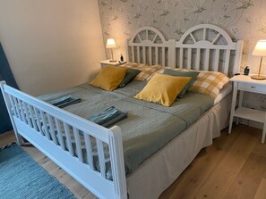 A bed with a white headboard, two bedside tables, and a floral wallpaper pattern. - Gård Halltorps Hage (Borgholm)
