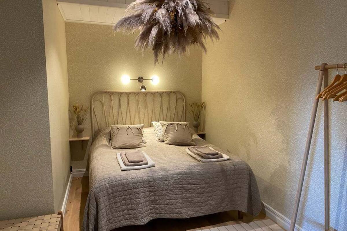 A bedroom with a bed, bedside tables, a hanging light fixture, and a wooden ladder.