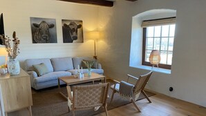 Una sala de estar con un sofá, dos sillas de madera, una mesita y un ventanal con vistas.