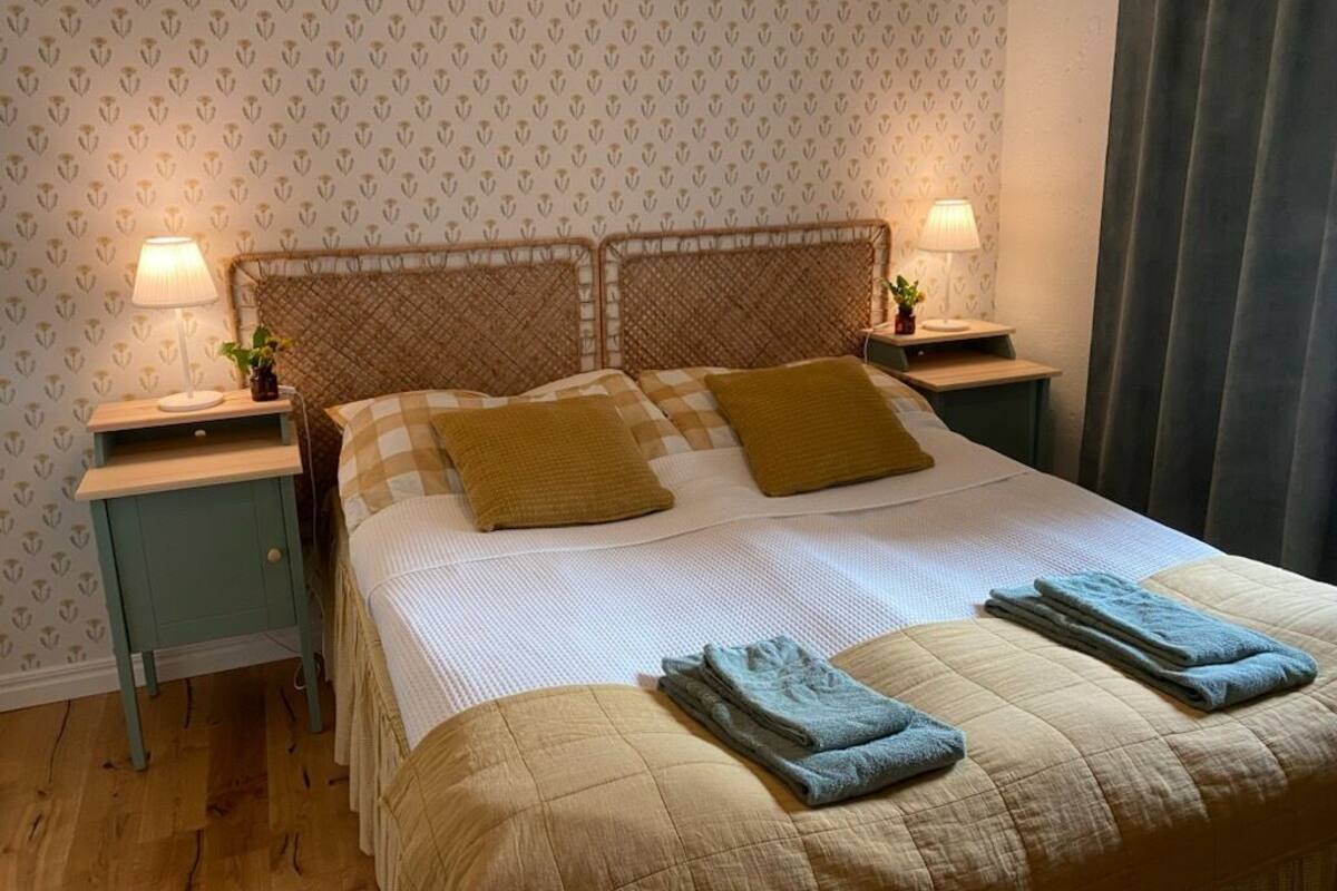 A neatly made bed with two pillows, a bedside table with a lamp, and a patterned wallpaper.