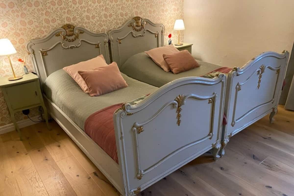A double bed with ornate headboard and footboard, two bedside tables with lamps, and a floral-patterned wallpaper.