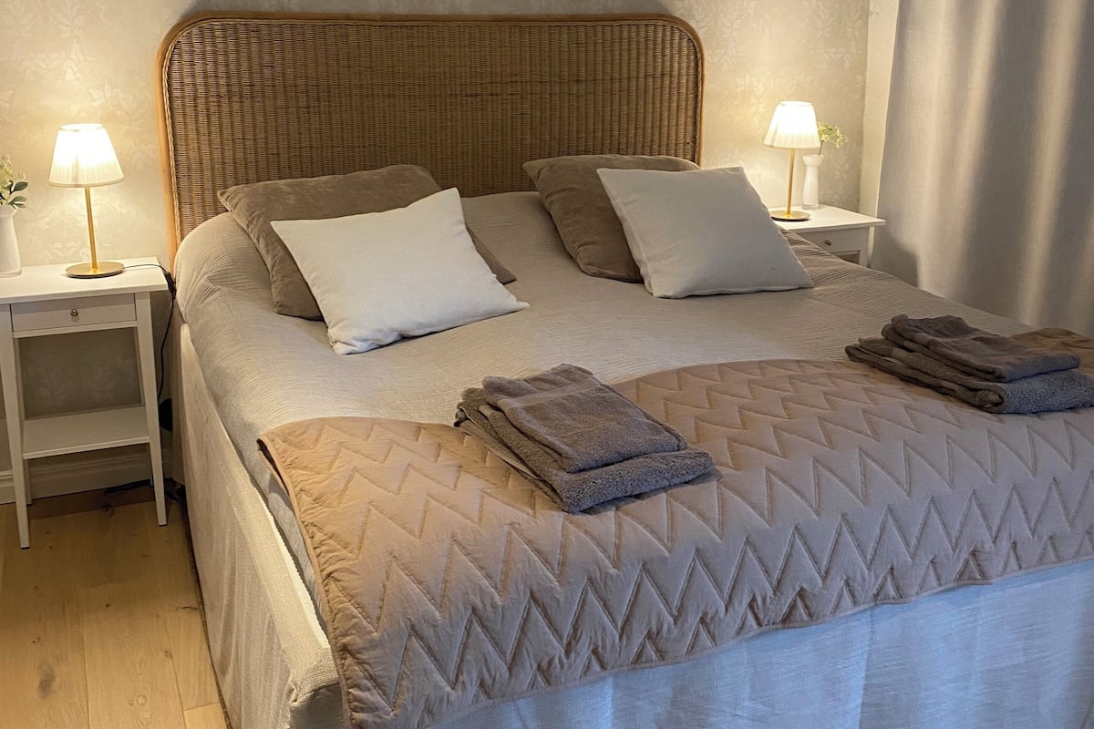 A neatly made bed with a quilted cover, two bedside tables with lamps, and a ceiling fan.