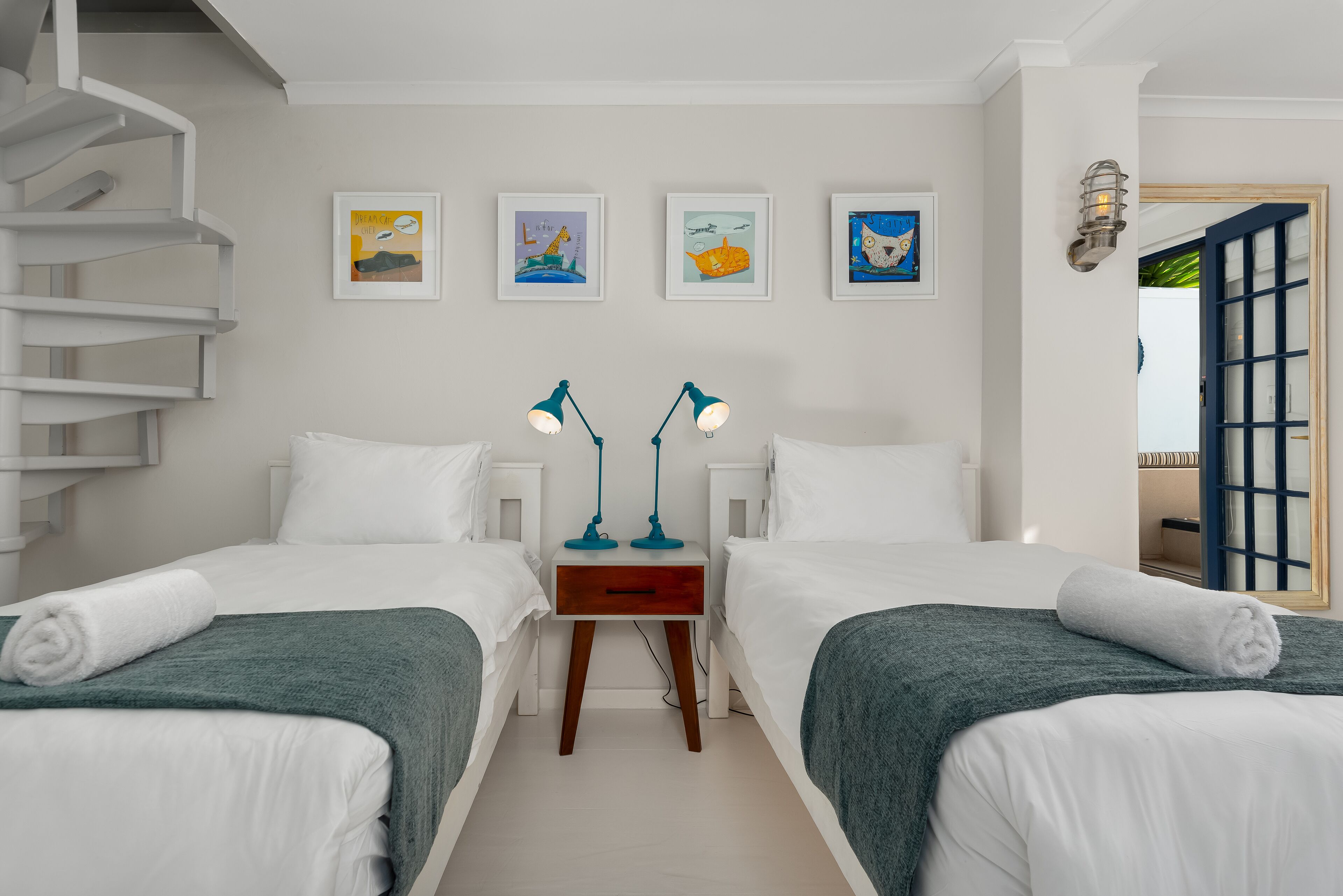 A hotel room with two beds, a wooden nightstand, two wall-mounted lamps, and four framed artworks on the wall.