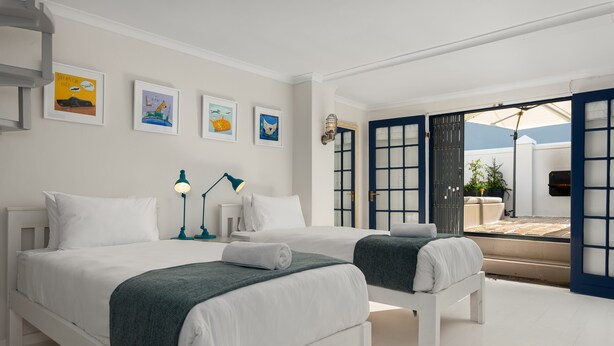 A hotel room with two beds, a desk, a lamp, and artwork on the walls. - Torbay 31 (Cape Town)