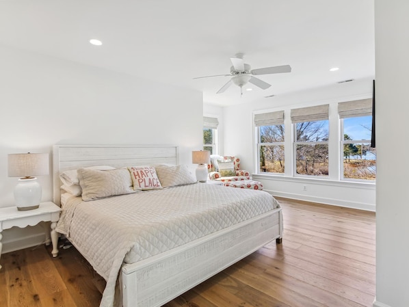 A bedroom with a bed, nightstands, a ceiling fan, and large windows.