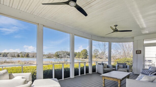 Un espacio exterior cubierto con una terraza de madera, muebles blancos y dos ventiladores de techo.