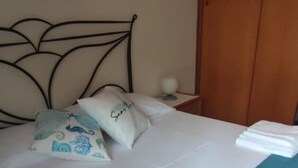 A neatly made bed with two decorative pillows, a bedside table with a lamp, and a wooden door in the background. - Villa Lucia Fontane Bianche (Fontane Bianche)