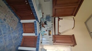 A kitchen with blue and white tiles, wooden cabinets, a white sink, and a countertop with various items. - Villa Lucia Fontane Bianche (Fontane Bianche)