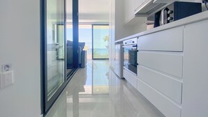 Une cuisine moderne avec des meubles blancs, une porte vitrée donnant sur un balcon et une vue sur l’extérieur.