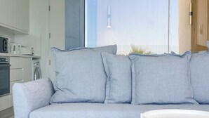 Un salon moderne avec un canapé gris, une table basse blanche et un coin cuisine à l’arrière-plan.