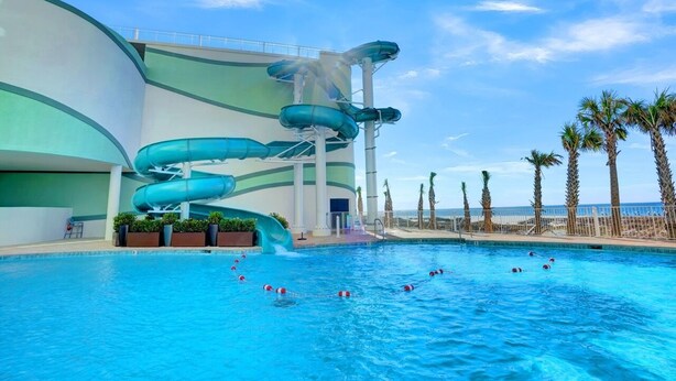 A pool area with a water slide and palm trees. - Turquoise Place 2402C by Liquid Life (Orange Beach)