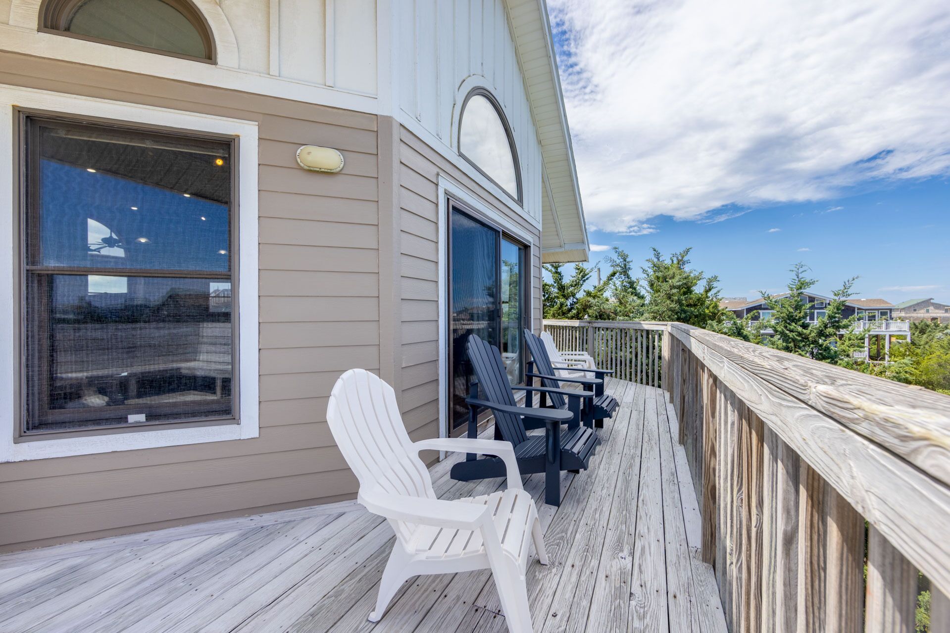 Um deck de madeira com duas cadeiras Adirondack e uma mesa, com vista para uma área residencial.