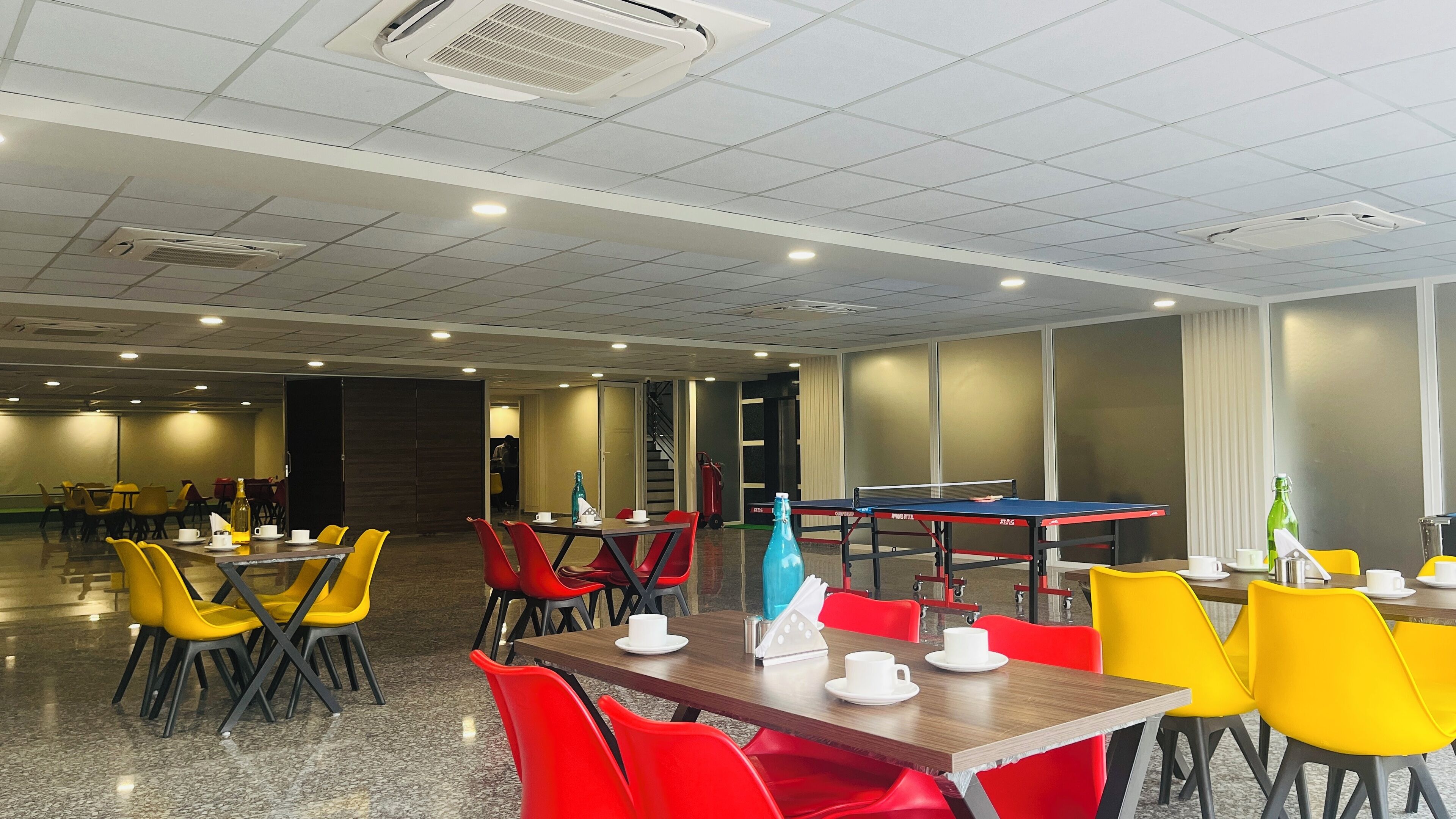 A spacious indoor dining area with multiple tables and chairs, a ping pong table, and a fire extinguisher.