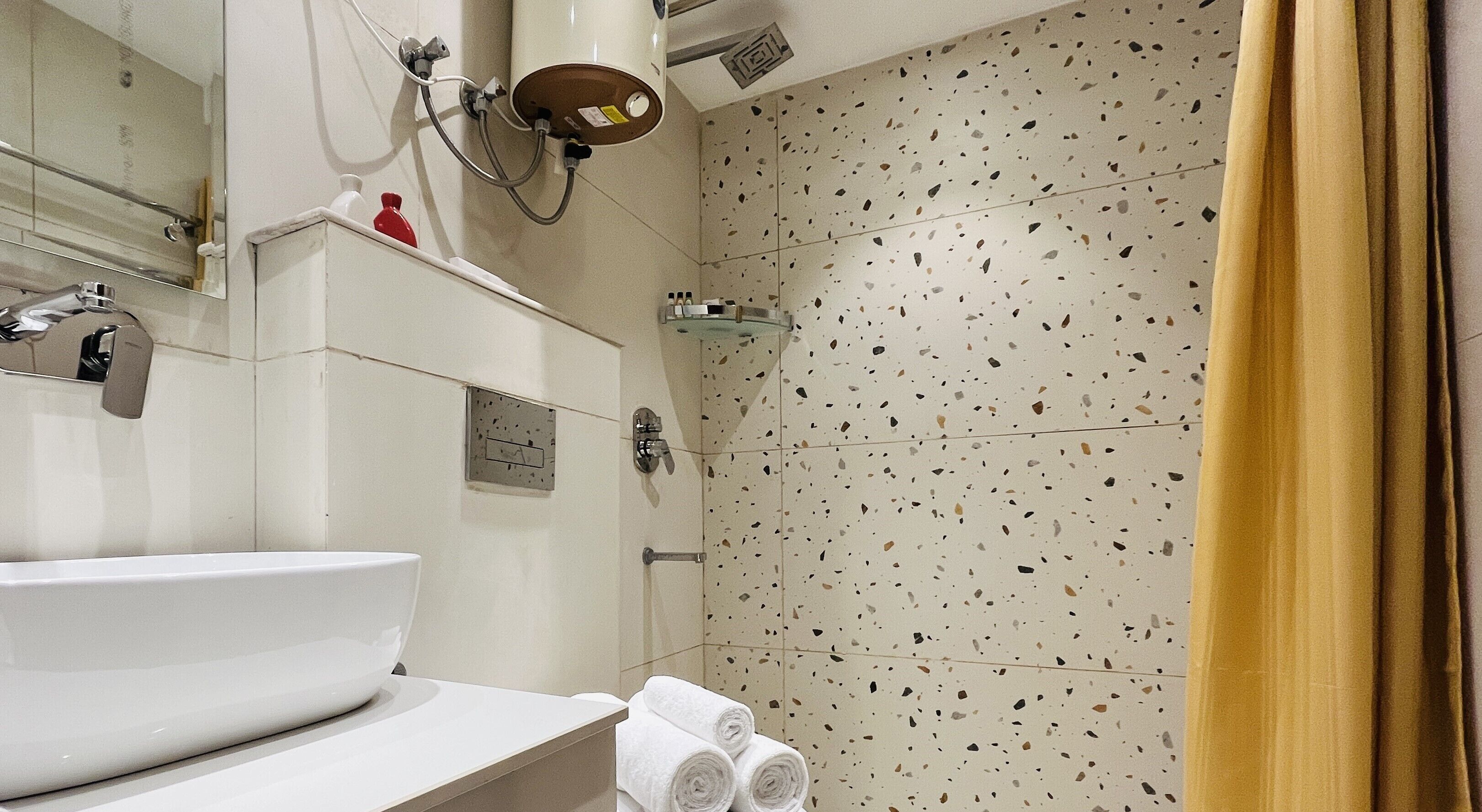 Une salle de bain avec un lavabo blanc, une cabine de douche en verre et un mur recouvert de carreaux à motifs.