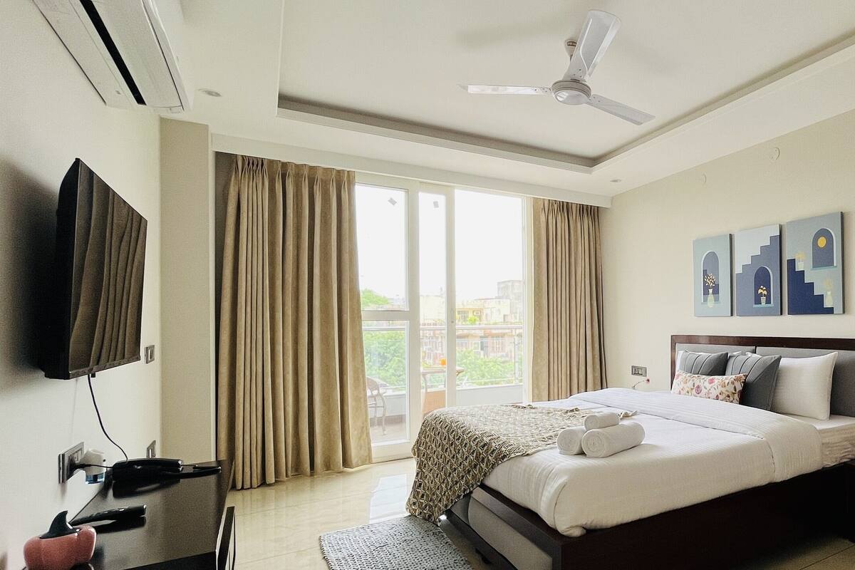 A hotel room with a bed, a flat-screen TV, a desk with a phone, and a ceiling fan.