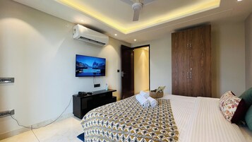 Une chambre d’hôtel moderne dotée d’un grand lit, d’un téléviseur à écran plat fixé au mur, d’un ventilateur de plafond et d’une armoire en bois.