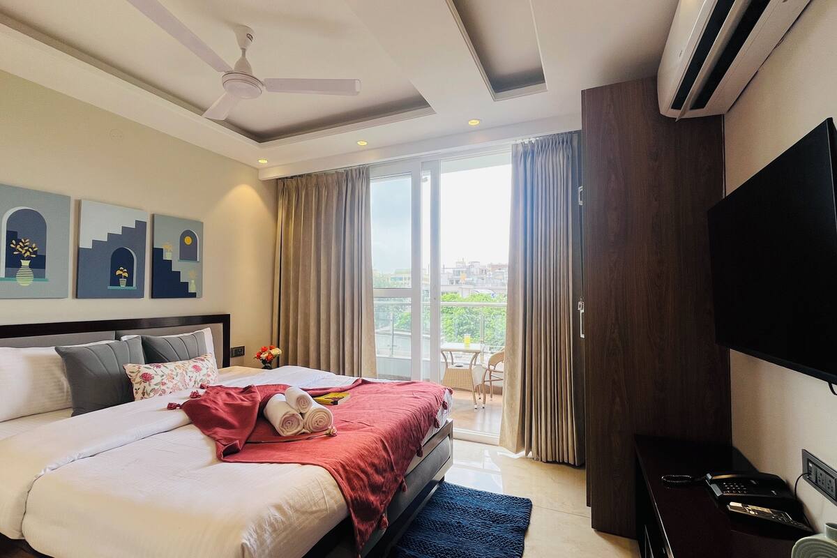 A hotel room with a bed, a ceiling fan, a TV, and a balcony with curtains.
