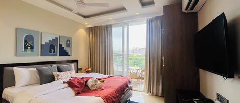 A hotel room with a bed, a ceiling fan, a TV, and a balcony with curtains.