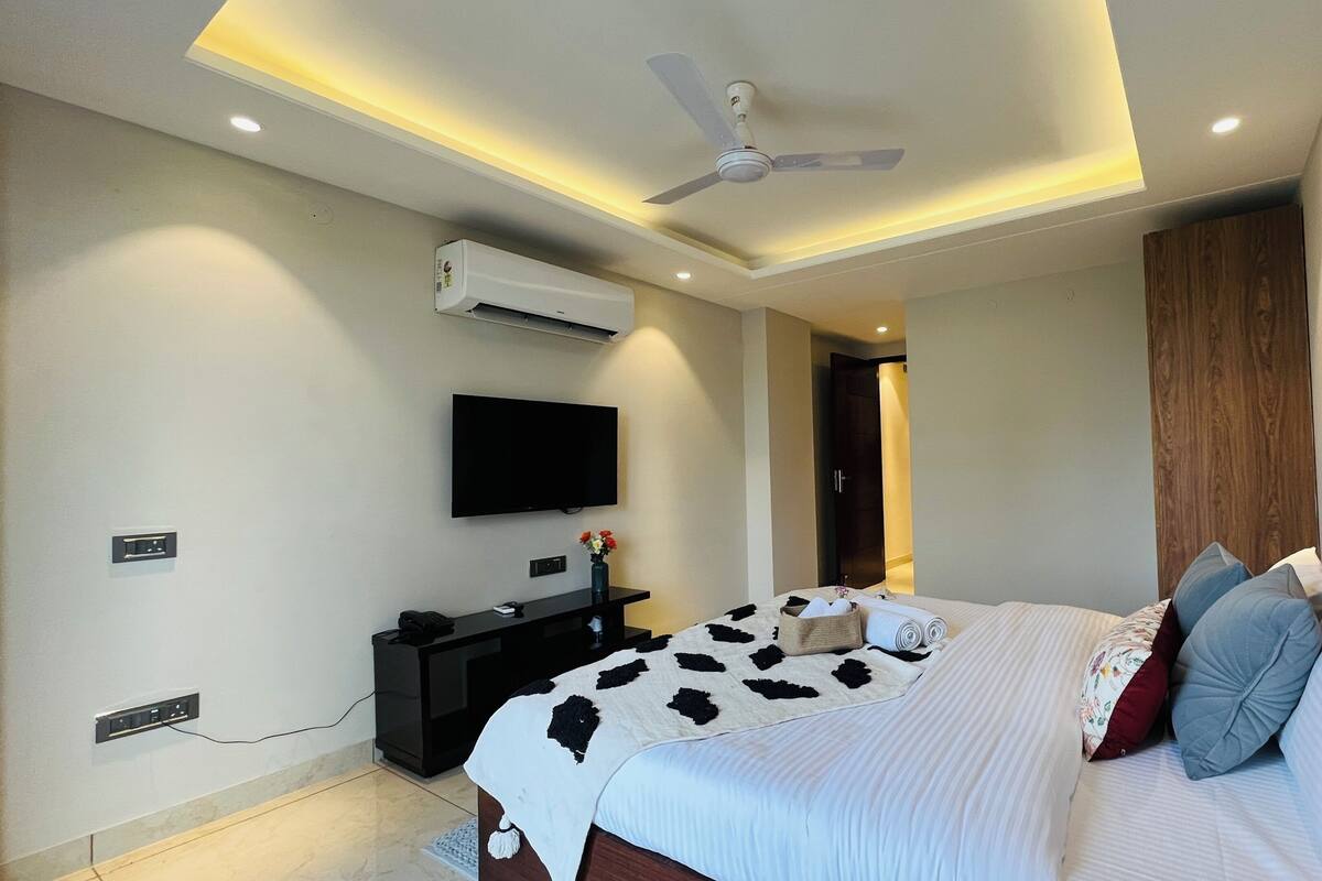 A modern bedroom with a bed, a flat-screen TV, a ceiling fan, and an air conditioning unit.
