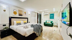 Una habitación de hotel moderna con una cama grande, un sofá verde, un televisor de pantalla plana y obras de arte en las paredes.