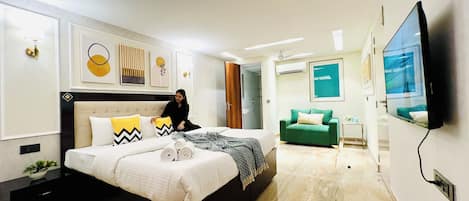 A modern bedroom with a bed, a green armchair, a TV, and artwork on the walls.