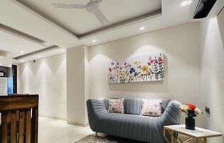 A modern living room with a grey sofa, a wooden dining table, and a ceiling fan.